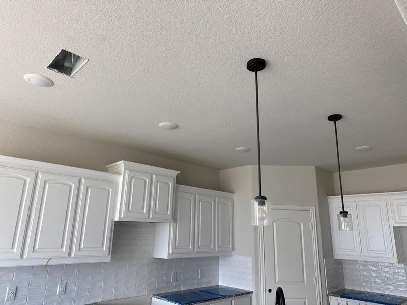 Kitchen featuring white cabinetry, subway tile backsplash, recessed lighting, and two pendant lights with clear glass shades