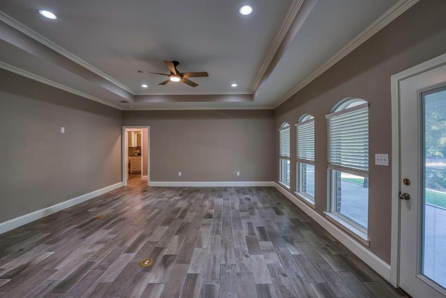 Family room with a tray ceiling, ceiling fan, wood tile flooring, and crown molding and great view of the covered and screened porch providing passive heat in winter and summer