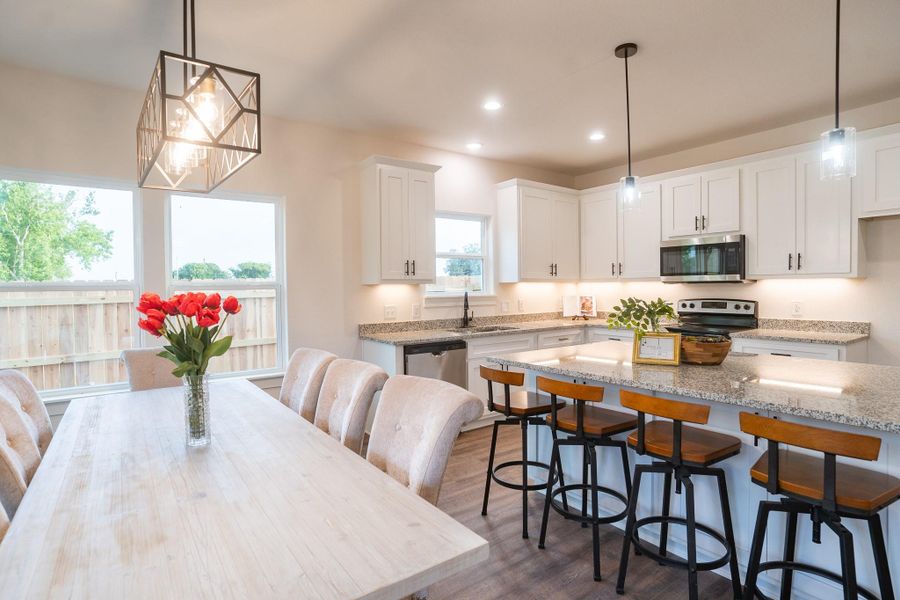 Kitchen with appliances with stainless steel finishes, a sink, white cabinetry, light stone countertops, and dark wood-type flooring