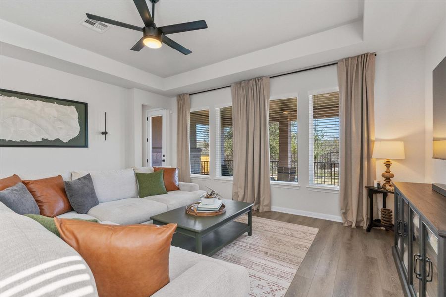 Living room featuring a tray ceiling, ceiling fan, and light wood finished floors