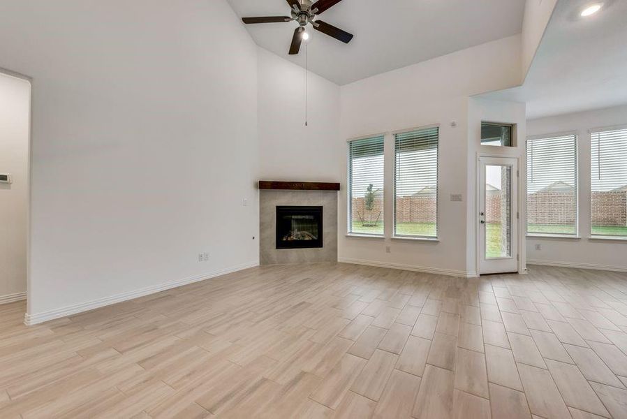 Unfurnished living room featuring a fireplace, high vaulted ceiling, light hardwood / wood-style flooring, and ceiling fan