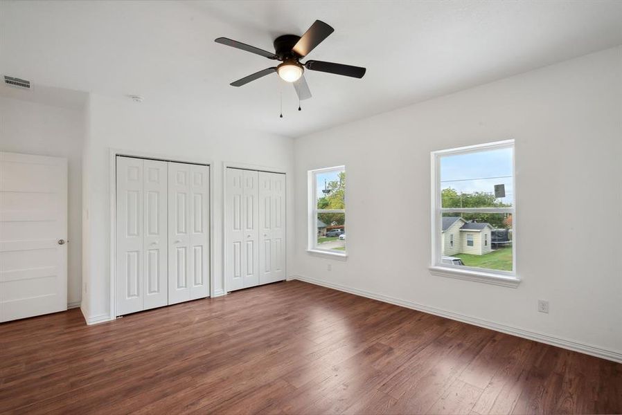 Unfurnished bedroom with ceiling fan, multiple closets, and dark hardwood / wood-style flooring