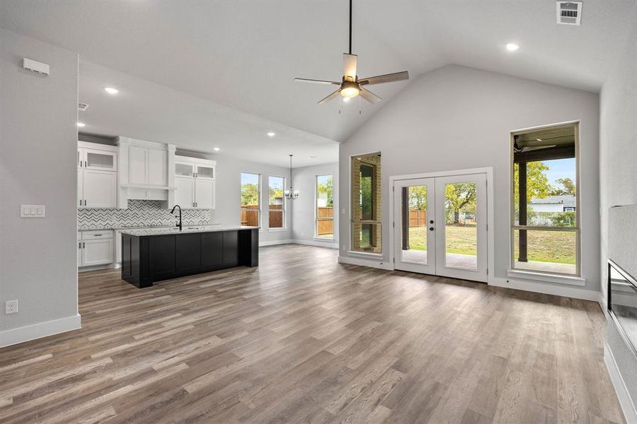 Unfurnished living room with light wood-style floors, recessed lighting, ceiling fan, high vaulted ceiling, and french doors