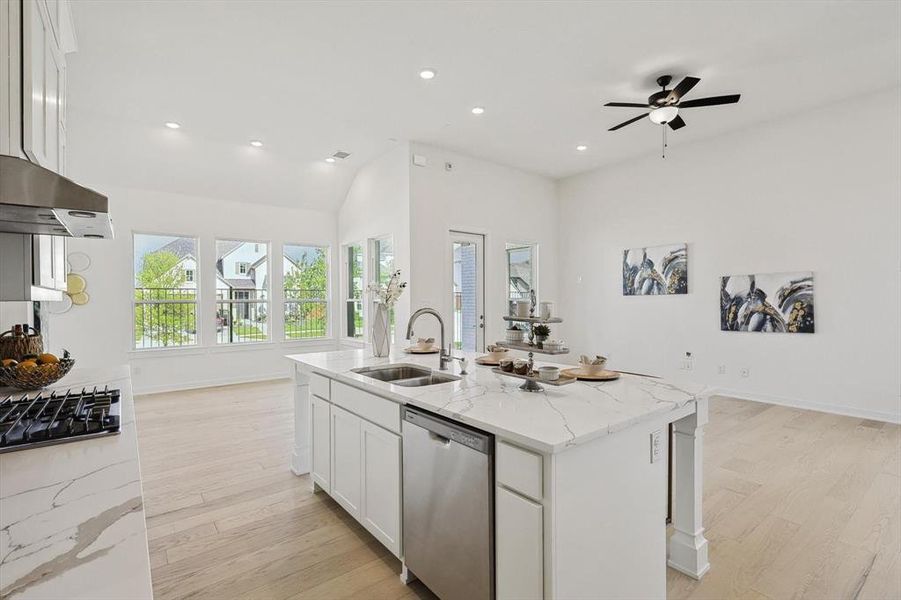 Kitchen featuring white cabinets, an island with sink, stainless steel dishwasher, light hardwood / wood-style flooring, and light stone countertops