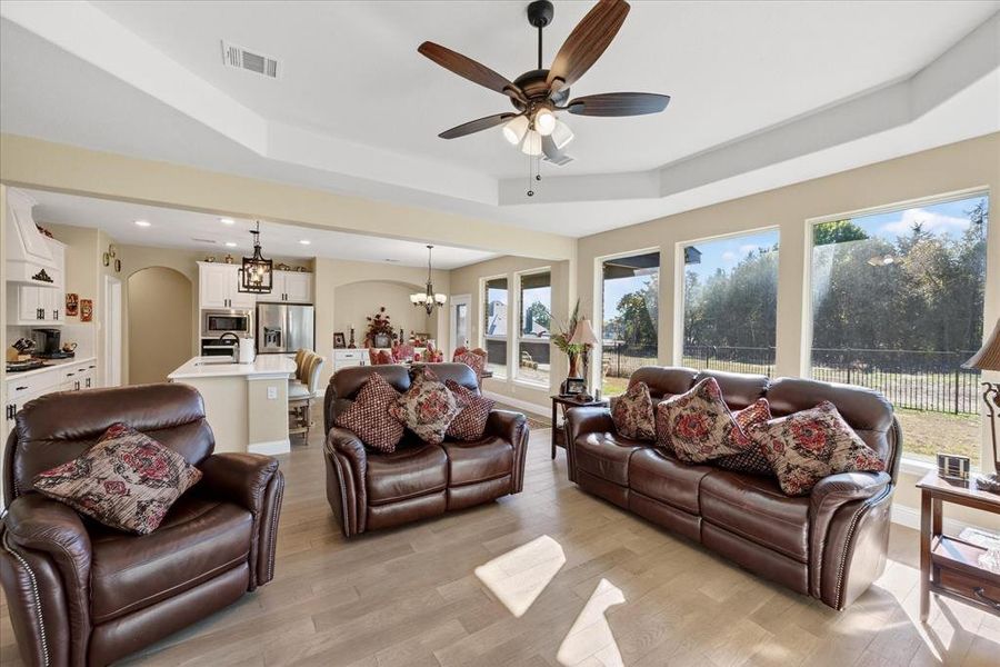 Living area featuring a chandelier, a raised ceiling, ceiling fan, light wood-style floors, and arched walkways Living area featuring a chandelier, a raised ceiling, ceiling fan, light wood-style floors, and arched walkways