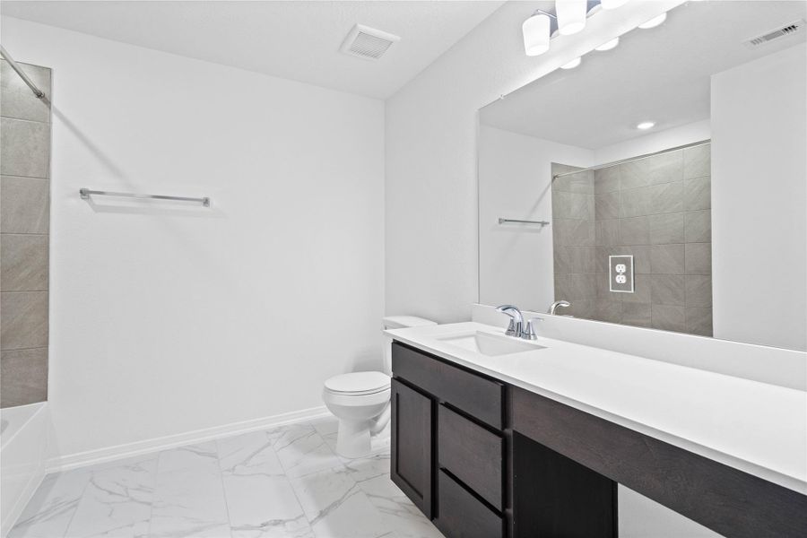 The secondary bathroom offers tile flooring, a bath/shower combination with a stylish tile surround, rich stained wood cabinetry with added knee space and elegant light countertops, a mirror, and sleek fixtures with modern finishes. The secondary bathroom offers tile flooring, a bath/shower combination with a stylish tile surround, rich stained wood cabinetry with added knee space and elegant light countertops, a mirror, and sleek fixtures with modern finishes.