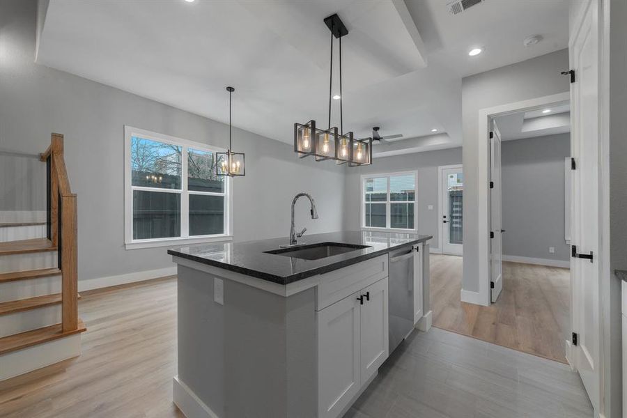 Kitchen with a sink, dark stone counters, an inviting chandelier, white cabinetry, and stainless steel dishwasher