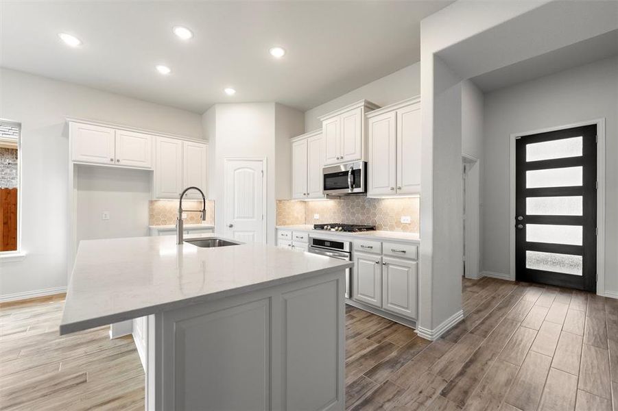 Kitchen with white cabinetry, light stone counters, a center island with sink, light wood finished floors, and recessed lighting