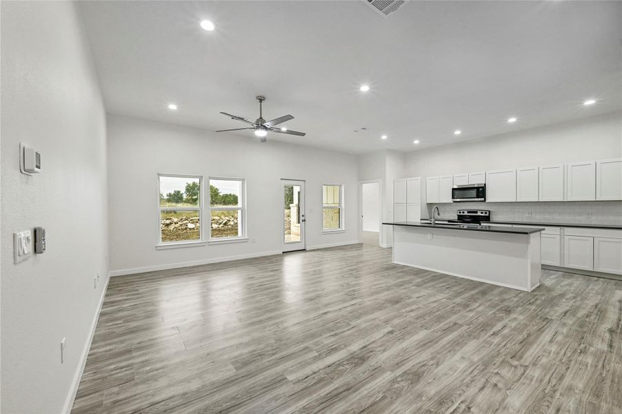 Kitchen with open floor plan, white cabinetry, dark countertops, a kitchen island with sink, and appliances with stainless steel finishes