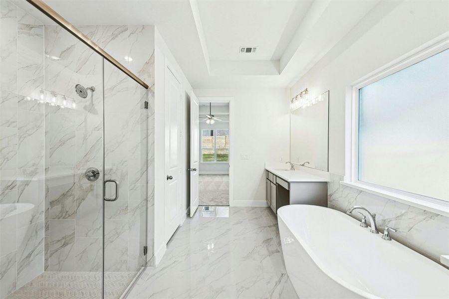 Full bath with a freestanding bath, light marble finish floors, vanity, a marble finish shower, and a tray ceiling