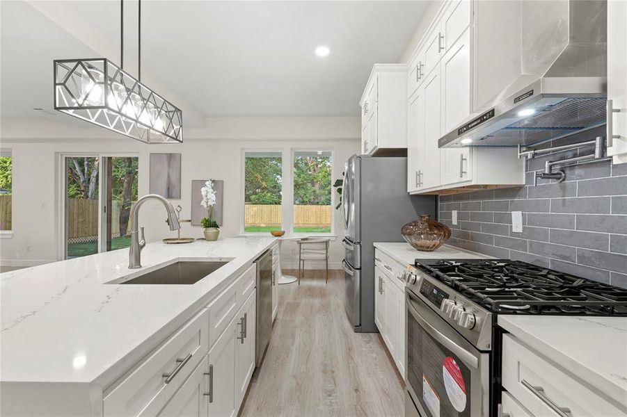 Kitchen featuring appliances with stainless steel finishes, wall chimney exhaust hood, plenty of natural light, light wood finished floors, and recessed lighting Kitchen featuring appliances with stainless steel finishes, wall chimney exhaust hood, plenty of natural light, light wood finished floors, and recessed lighting