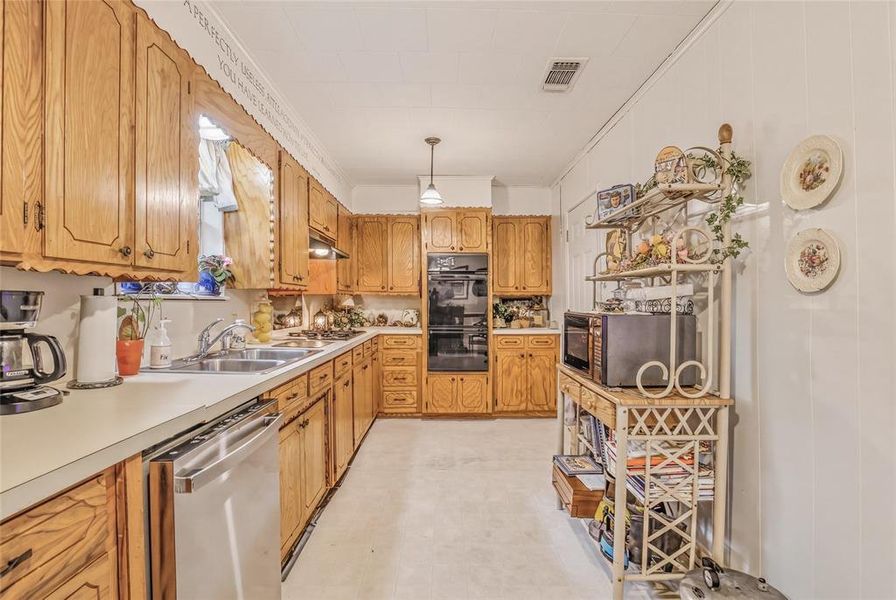 U-shaped kitchen featuring wood cabinetry, built-in double ovens, white countertops, and a double basin stainless steel sink U-shaped kitchen featuring wood cabinetry, built-in double ovens, white countertops, and a double basin stainless steel sink