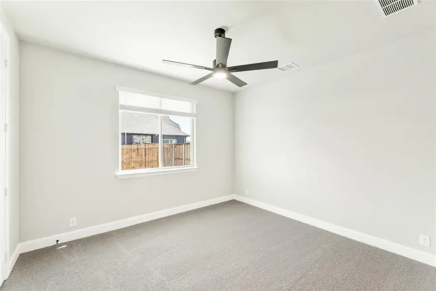 Empty bedroom with gray carpet, ceiling fan, and single window with backyard view Empty bedroom with gray carpet, ceiling fan, and single window with backyard view