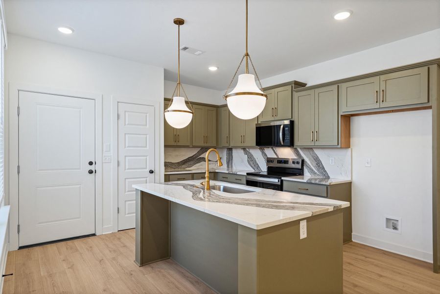 Modern kitchen featuring a central island with a waterfall-edge countertop, two pendant lights, wood-finish flooring, and sage green cabinetry with stainless steel hardware Modern kitchen featuring a central island with a waterfall-edge countertop, two pendant lights, wood-finish flooring, and sage green cabinetry with stainless steel hardware