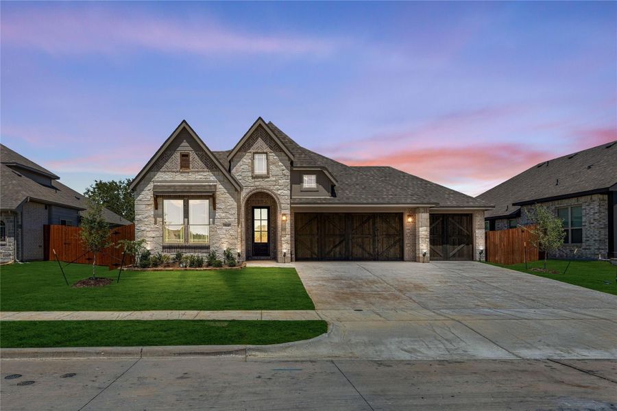 Single-story home with stone and brick exterior, two-car garage with wood doors, and manicured front lawn at dusk