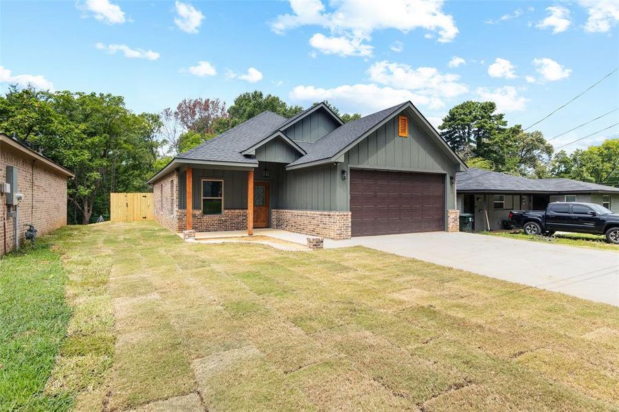 View of front facade with brick siding, a garage, driveway, board and batten siding, and a shingled roof