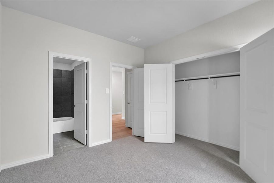 Unfurnished bedroom featuring light colored carpet, a closet, ensuite bath, and light tile patterned flooring Unfurnished bedroom featuring light colored carpet, a closet, ensuite bath, and light tile patterned flooring
