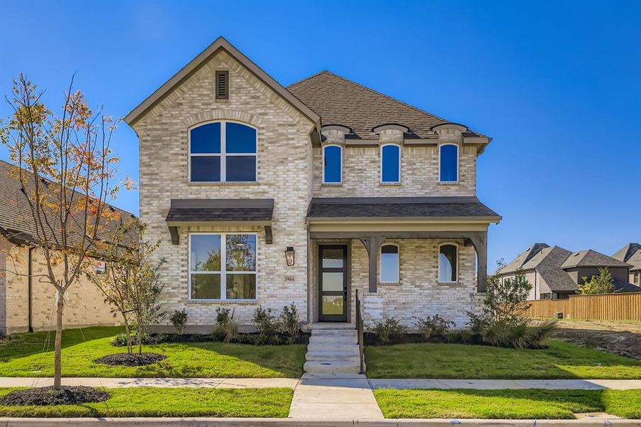 French country inspired facade with brick siding, a porch, and roof with shingles French country inspired facade with brick siding, a porch, and roof with shingles