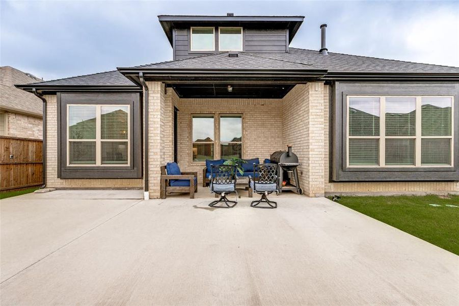 Expansive concrete patio area featuring a covered porch, brick exterior, and a secondary story dormer with windows