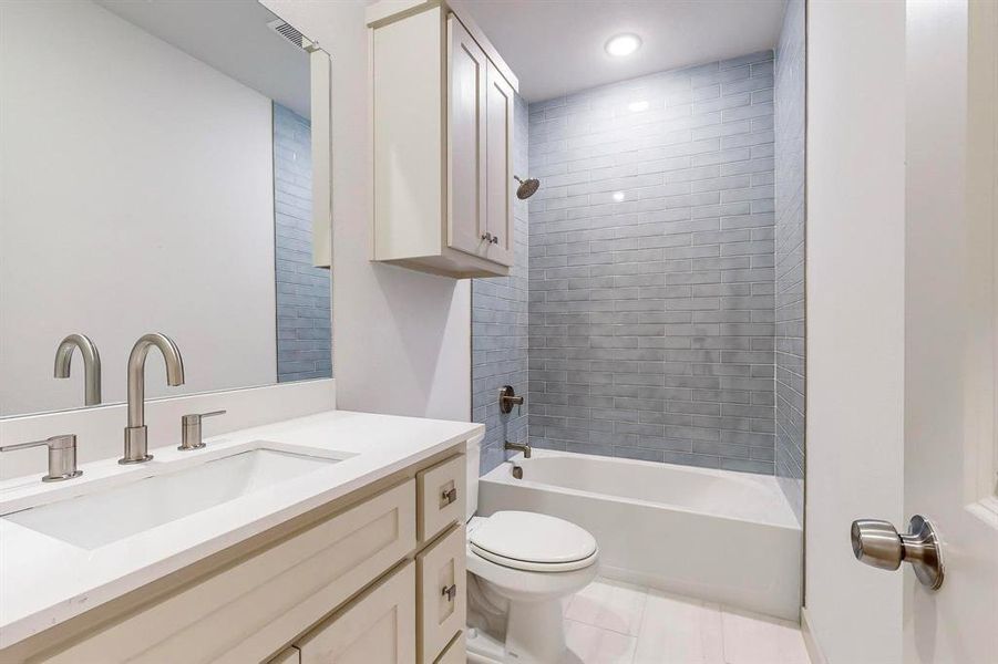 Full bathroom with toilet, tiled shower / bath combo, vanity, and tile patterned floors