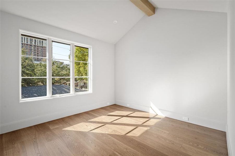 Bathed in natural sunlight, this secondary bedroom boasts an airy atmosphere with expansive windows that frame scenic neighborhood views. A vaulted ceiling with a stained wood beam adds architectural interest, while white oak hardwood floors provide a warm and timeless foundation.