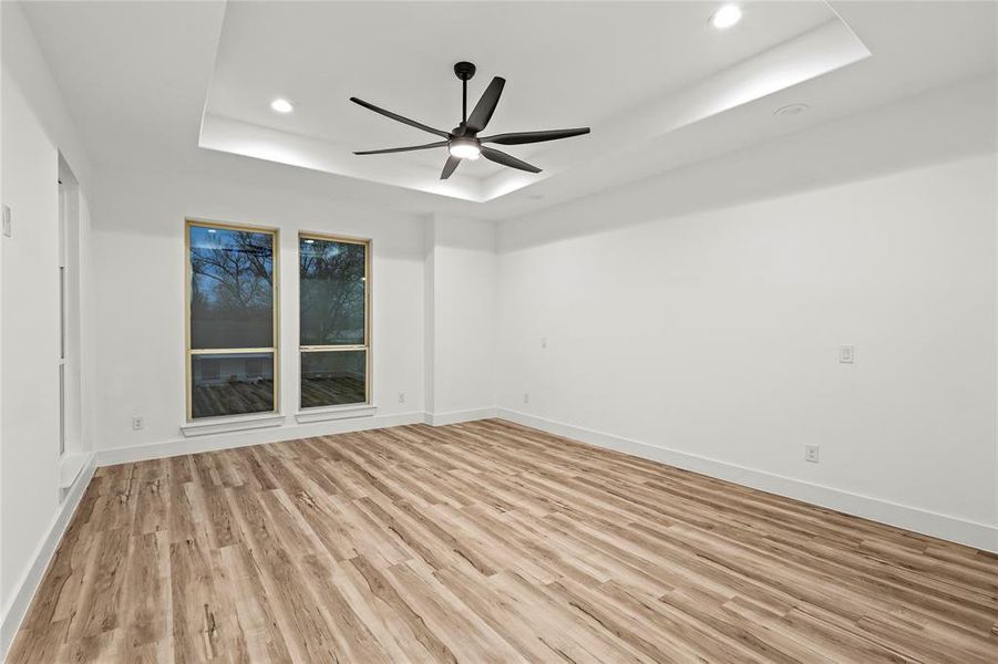 Empty room with a raised ceiling, ceiling fan, and light wood-type flooring