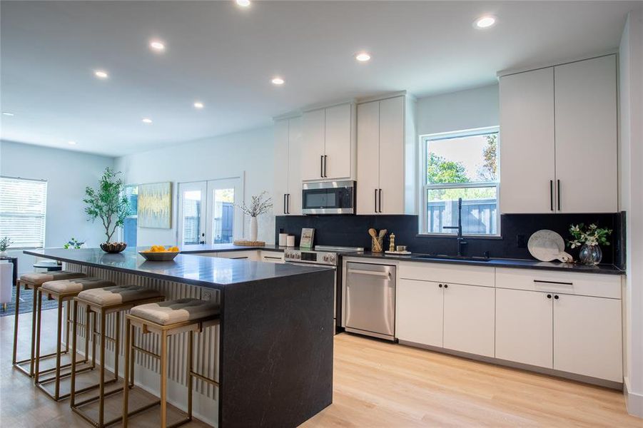 Kitchen with appliances with stainless steel finishes, light wood-type flooring, a center island, and white cabinetry