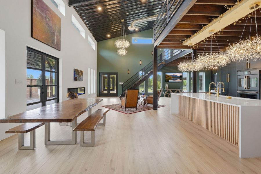 This modern, open-concept space features high ceilings, large windows, and sleek finishes. A spacious kitchen island with unique lighting, a wooden dining table, and a stylish staircase create an inviting atmosphere. Perfect for contemporary living.