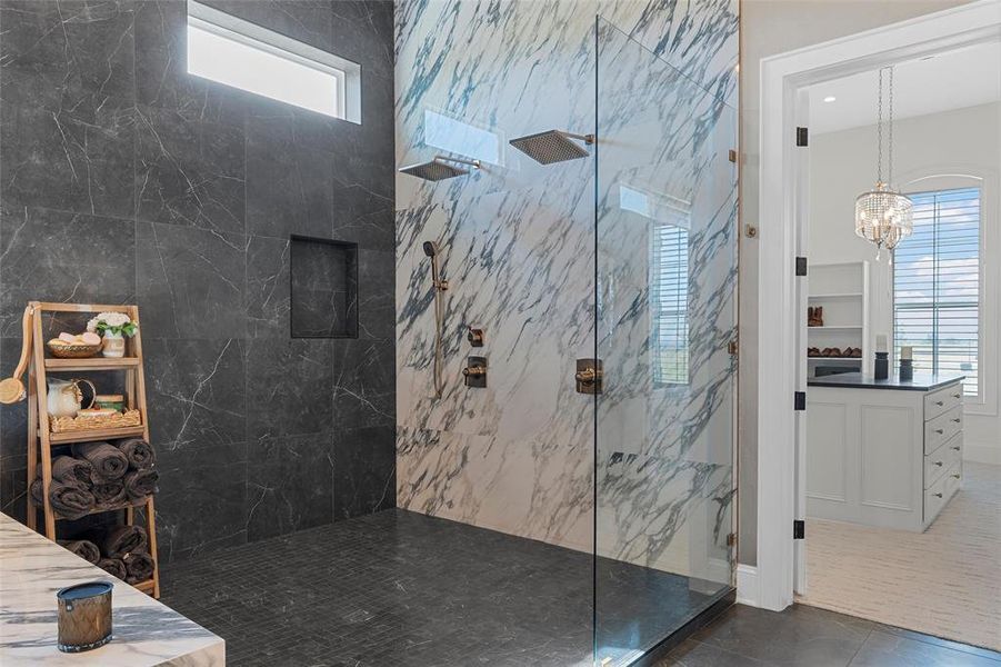 Full bath featuring a marble finish shower, dark tile patterned flooring, and a chandelier