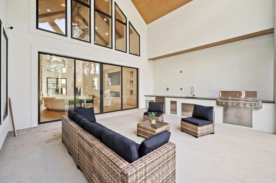 Covered outdoor living area featuring vaulted wood ceiling accents and fully equipped outdoor kitchen.