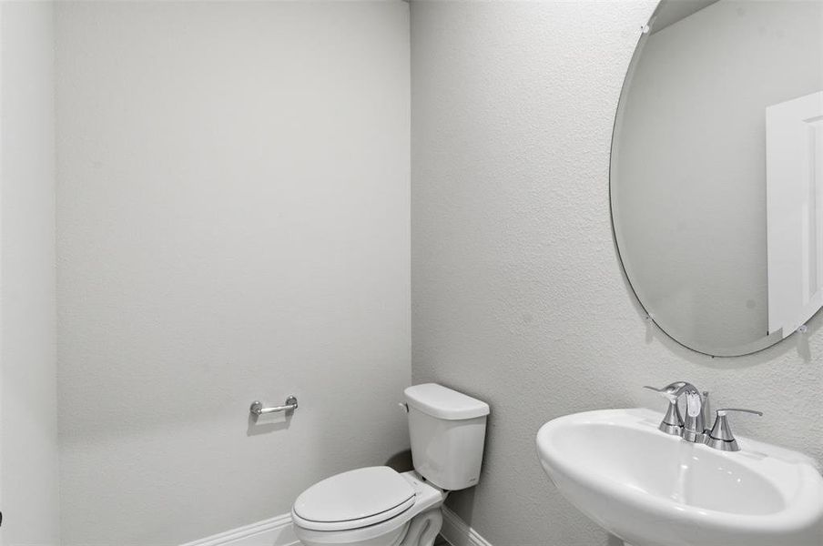 Bathroom featuring a pedestal sink with a chrome faucet, a white toilet, and a circular mirror