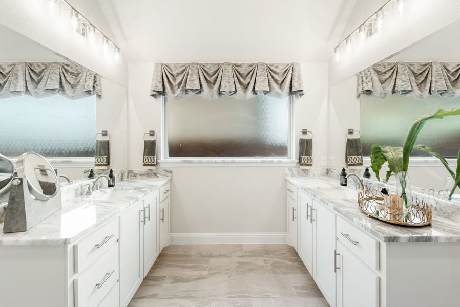 Bathroom with dual vanities, white cabinets, marble countertops, and a frosted privacy window between them
