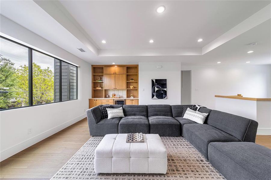 Living area featuring bar with sink, a raised ceiling, light wood-type flooring, recessed lighting, and beverage cooler