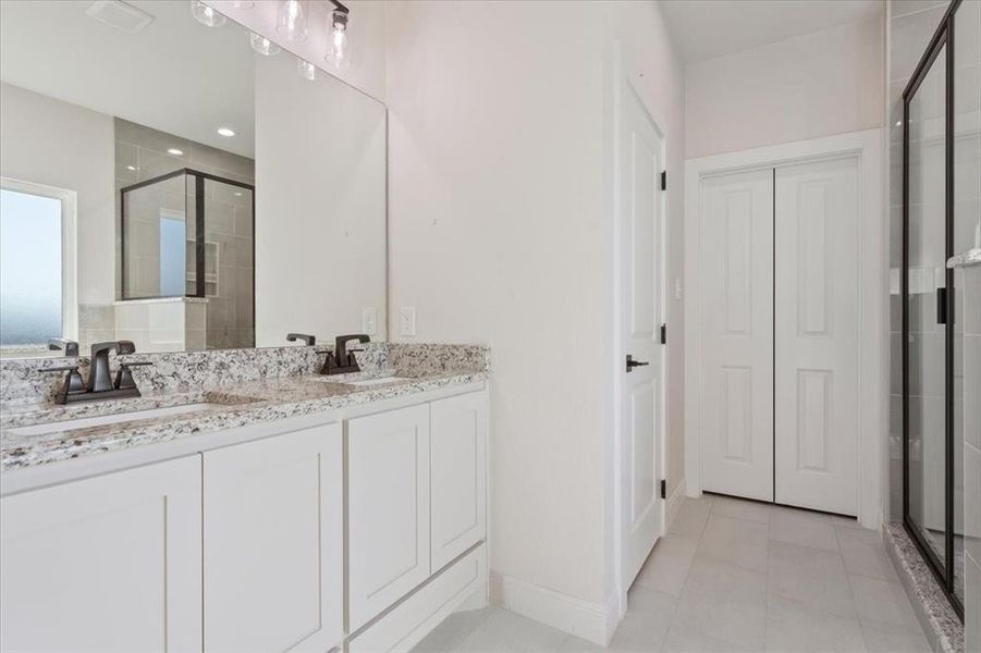 Bathroom featuring a shower stall, double vanity, light tile patterned floors, and a closet Bathroom featuring a shower stall, double vanity, light tile patterned floors, and a closet