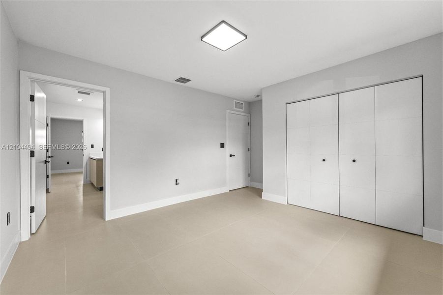 Neutral-toned interior space featuring light-colored tile flooring, flush-mount square ceiling lighting, and a multi-panel sliding closet system with matte black hardware