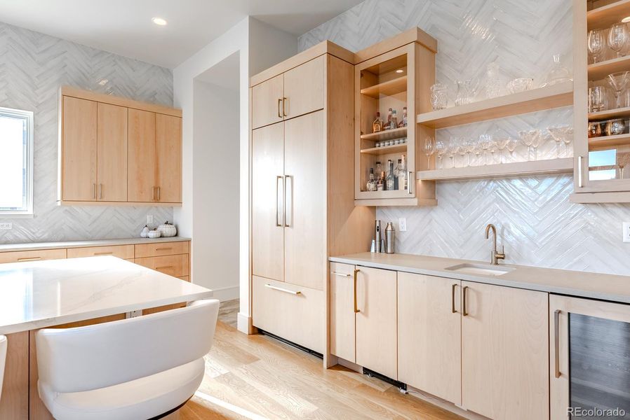 A complementary wet bar showcases glass front and open shelving, a dedicated wine refrigerator, and an ice maker—an entertainer’s dream poised between the kitchen and great room.
