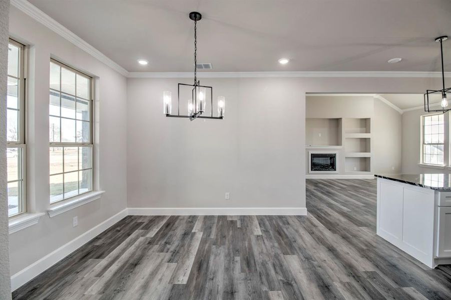 Unfurnished dining area featuring a chandelier, built in features, a glass covered fireplace, crown molding, and dark wood finished floors
