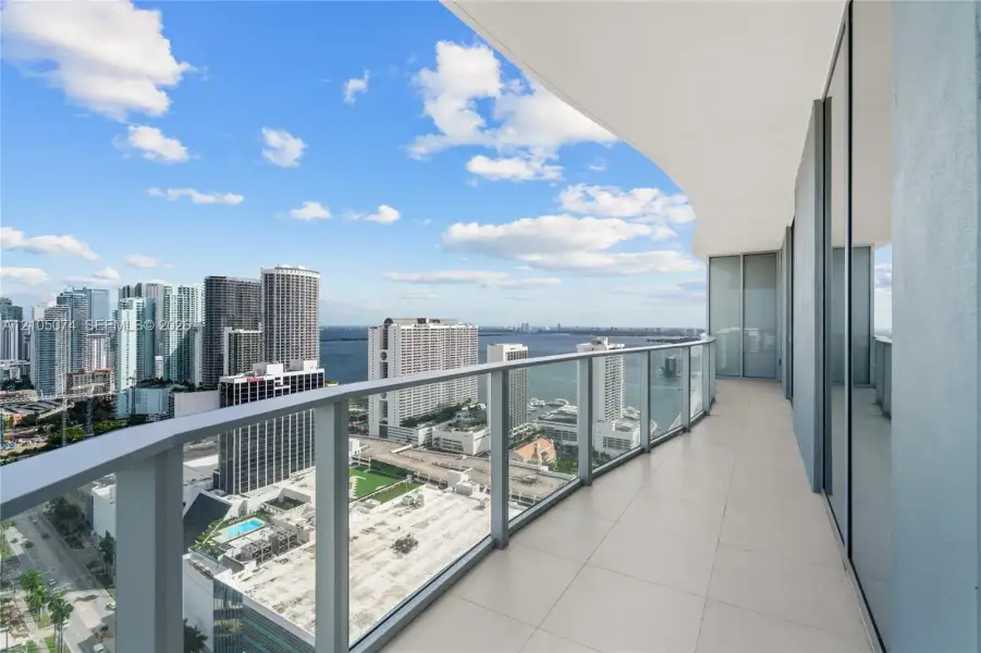 Wraparound balcony featuring large-format tile flooring, a glass panel railing, and full-height glass sliding door access