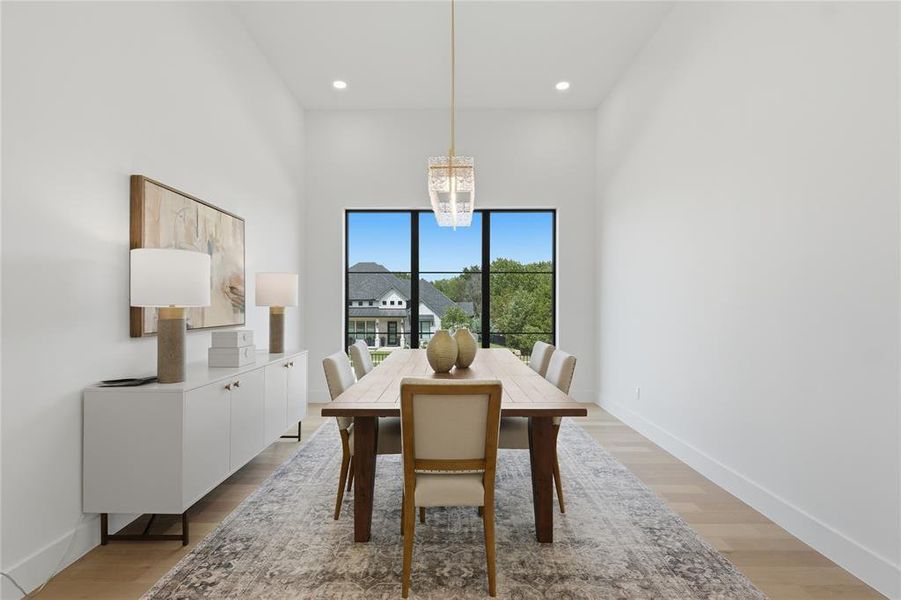 Dining area featuring high ceilings, light wood-finish flooring, a large window with dark trim, and a modern chandelier
