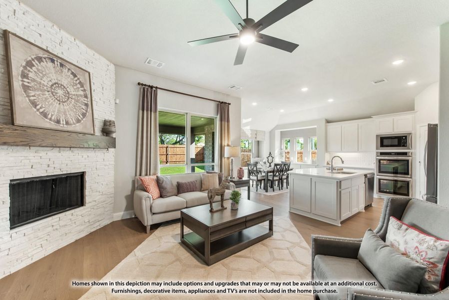 Open-concept living room with stone fireplace and ceiling fan, open to kitchen with island and dining area beyond