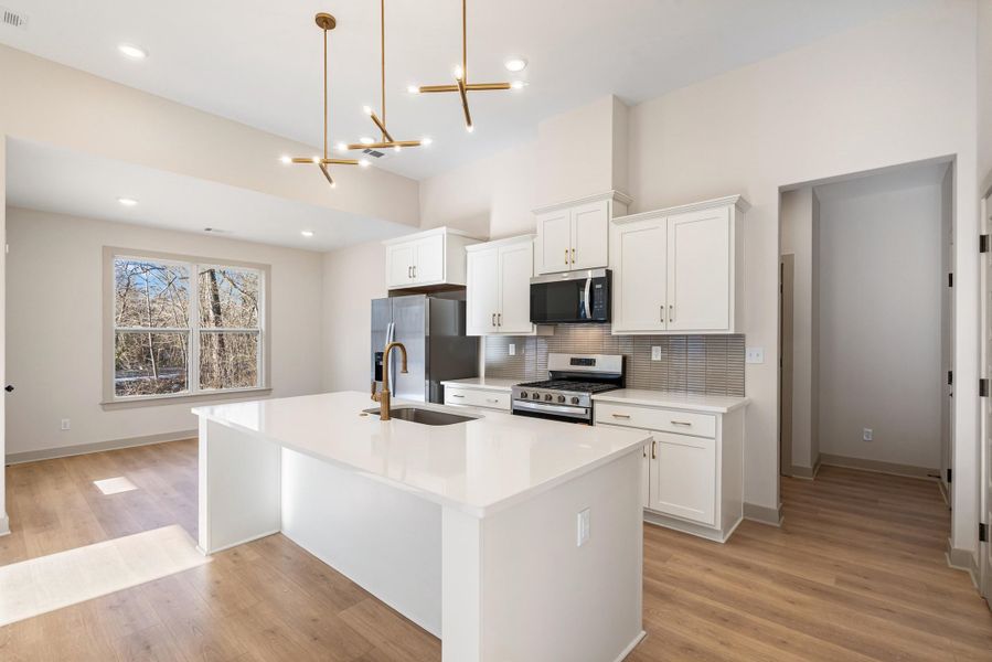 Kitchen with white cabinetry, stainless steel appliances, an island with sink, and suspended lighting