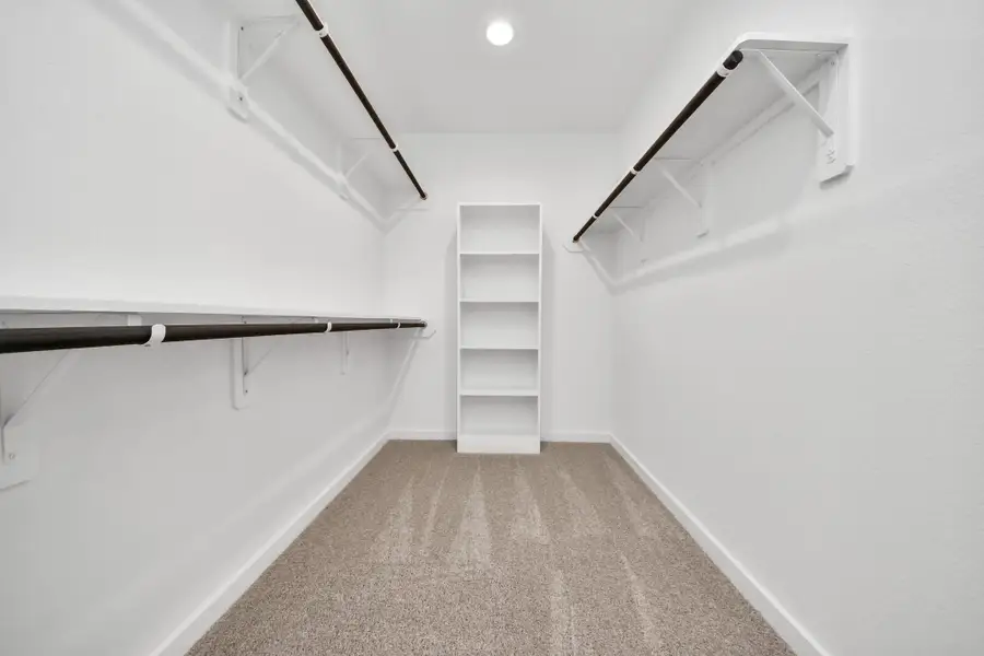 Walk-in closet that epitomizes luxury and practicality. This generously sized space features built-in shelving, offering abundant room for impeccable organization. High ceilings and recessed lighting create a bright and welcoming ambiance. Sample photo of completed home with similar floor plan. Actual colors and selections may vary.