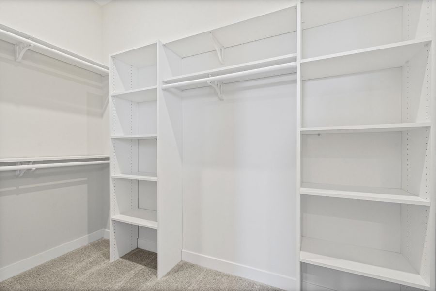 Walk-in closet featuring white built-in shelving, multiple hanging rods, and gray carpet flooring Walk-in closet featuring white built-in shelving, multiple hanging rods, and gray carpet flooring