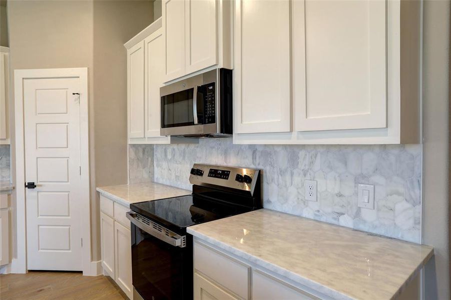 Kitchen featuring appliances with stainless steel finishes, decorative backsplash, white cabinets, light wood finished floors, and light stone counters