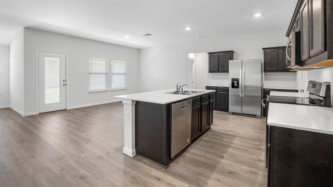 Kitchen with stainless steel appliances, a center island with sink, recessed lighting, and dark wood-type flooring