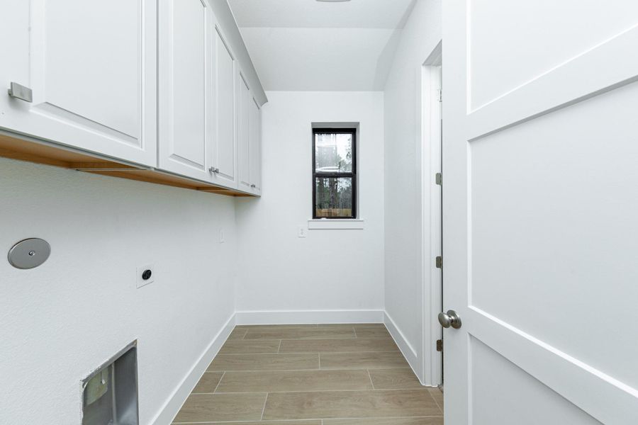 This bright and functional laundry room is conveniently located and ready for your appliances. It features clean white walls and trim, a window providing abundant natural light, and the gorgeous wood tile flooring for durability.