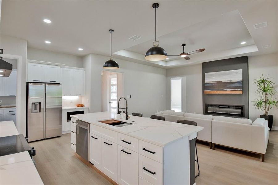 Kitchen with decorative light fixtures, white cabinetry, appliances with stainless steel finishes, a breakfast bar, and a raised ceiling Kitchen with decorative light fixtures, white cabinetry, appliances with stainless steel finishes, a breakfast bar, and a raised ceiling