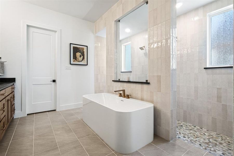 Full bath featuring walk in shower, a freestanding tub, vanity, and light tile patterned floors Full bath featuring walk in shower, a freestanding tub, vanity, and light tile patterned floors