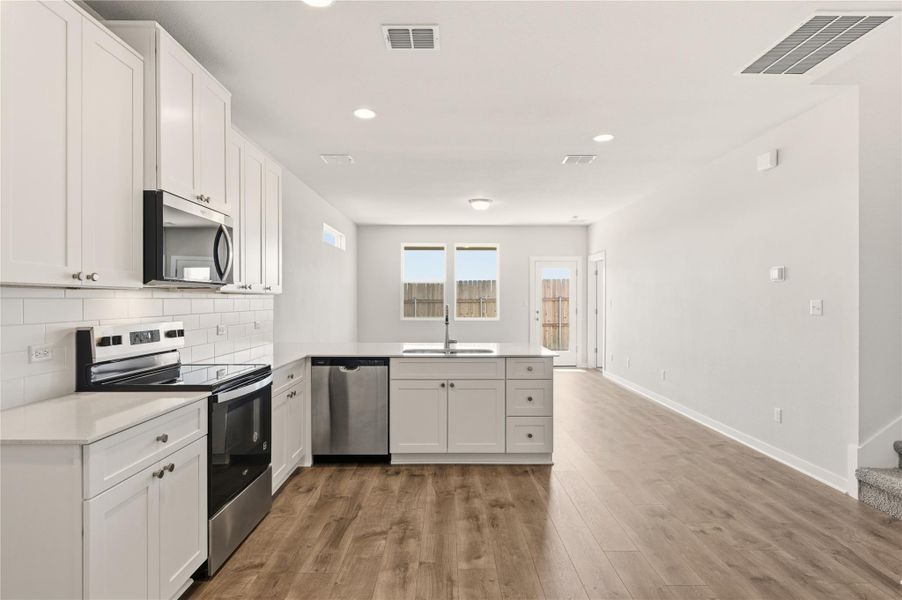 Kitchen featuring stainless steel appliances, a peninsula, white cabinetry, recessed lighting, and light wood-style floors