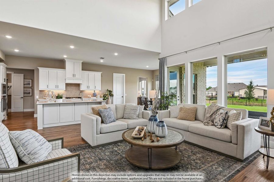 Open-concept living room with high ceilings, hardwood floors, and view into white kitchen with island Open-concept living room with high ceilings, hardwood floors, and view into white kitchen with island